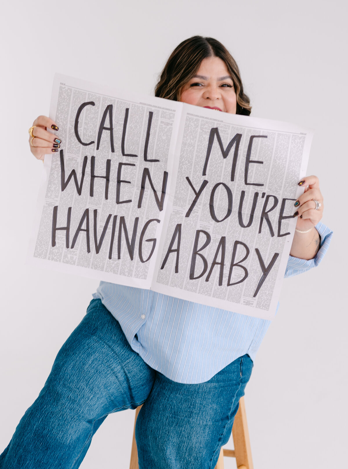 Melanie holding up a newspaper that reads "Call me when you're having a baby"